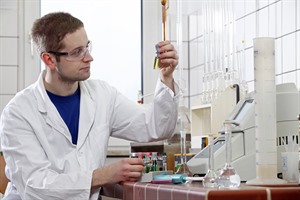 Ein Mitarbeiter analysiert Proben im Labor. Er hält ein Reagenzglas hoch.