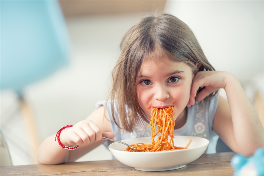 Ein Mädchen sitzt am Tisch und isst Spaghetti
