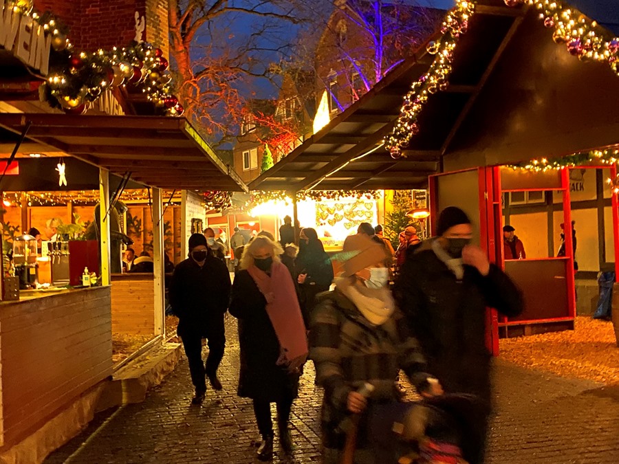 Menschen laufen über den Weihnachtsmarkt, vorbei an weihnachtlich geschmückten Buden.