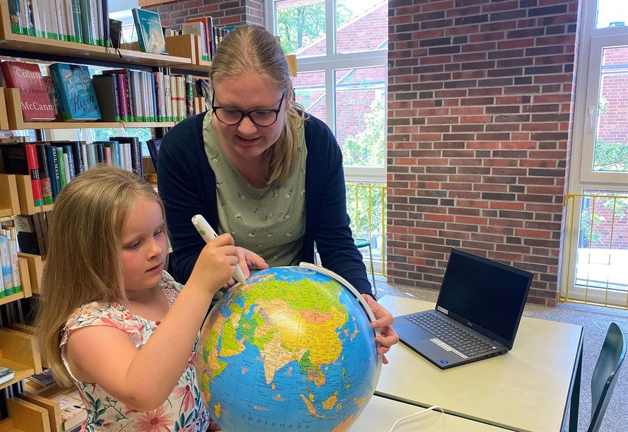 Juli Helms testet einen interaktiven Globus gemeinsam mit Jasmin Lührsen, Mitarbeiterin der Stadtbücherei. 