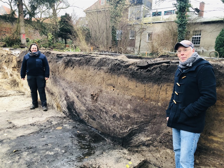 Daniela Kelm und Dr. Mathias Hensch stehen an dem jüngeren, etwa fünf Meter breiten Stadtgrabens. Verschiedene Erdschichten sind zu erkennen.