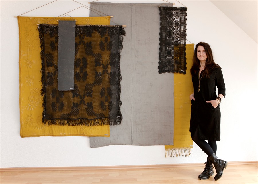 Eine Frau steht vor einem Kunstwerk, welches auf verschiedenen Textilien besteht
