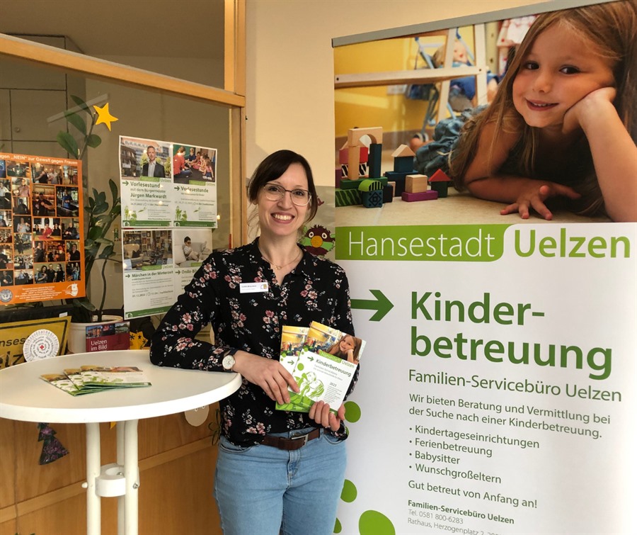 Judith Bräunlich steht an einem Stehttisch vor einem Rollup, auf dem das Hansestadt Logo zu sehen ist, sowie der Schriftzug "Kinder-Betreuung Familien-Servicebüro Uelzen"